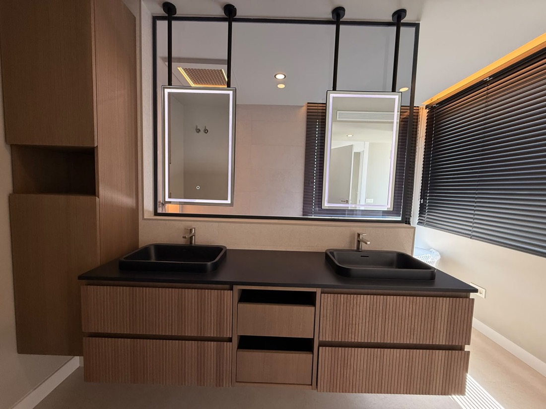 Doble lavabo con encimera de piedra negra y mueble de madera ranurada, espejos retroiluminados.